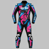 A full-body motorcycle racing suit from Aprilia, featuring a black base with vibrant pink and blue graphic patterns, white branding, and white shark illustrations, displayed against a solid gray background.